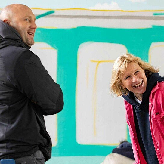 Roman Friedrich und Sylke Born lachen gemeinsam vor einem Graffiti-Kunstwerk