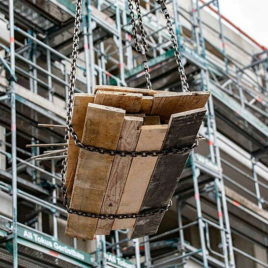 Holzpaneele fliegen mit Hilfe eines Baukrans über die Baustelle in Köln-Porz